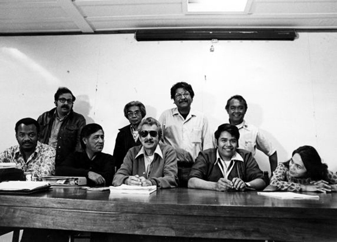 United Farm Worker officials sit and stand behind a table smiling for a photo.