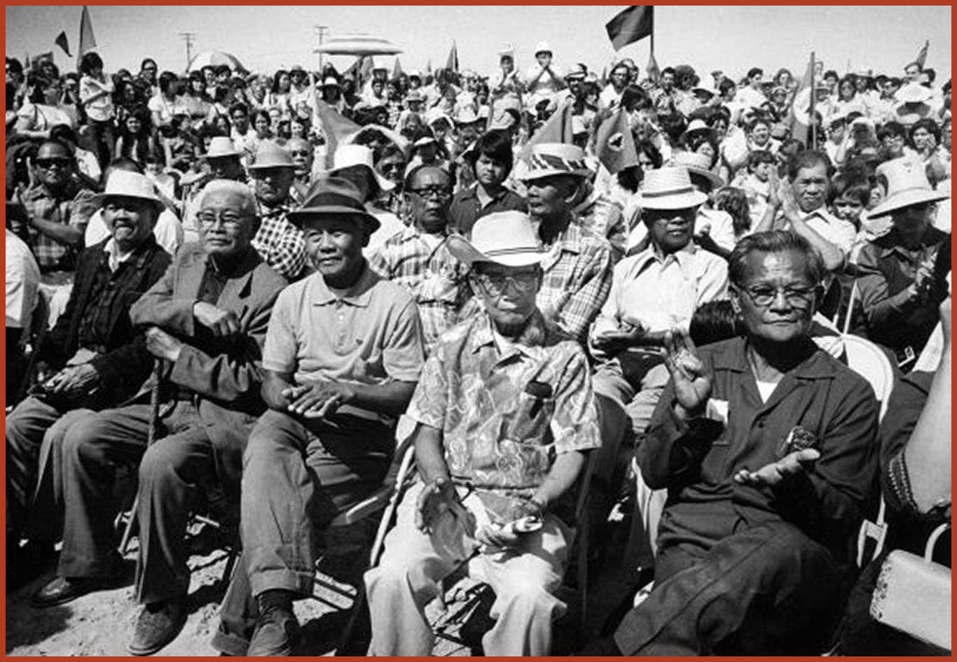 Large crowd of seated Filipino Farm Workers clapping and celebrating. There are flags and banners waving.