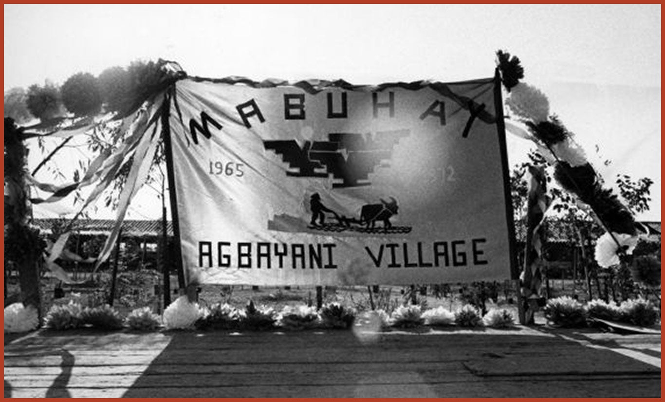 Large banner with the words "MABUHAY" written on the top and "Agbayani Village" on the bottom. In the middle is the UFW logo and the image of a man pushing a cart pulled the an ox. The year 1965 is written on the left and 1972 is written on the right.