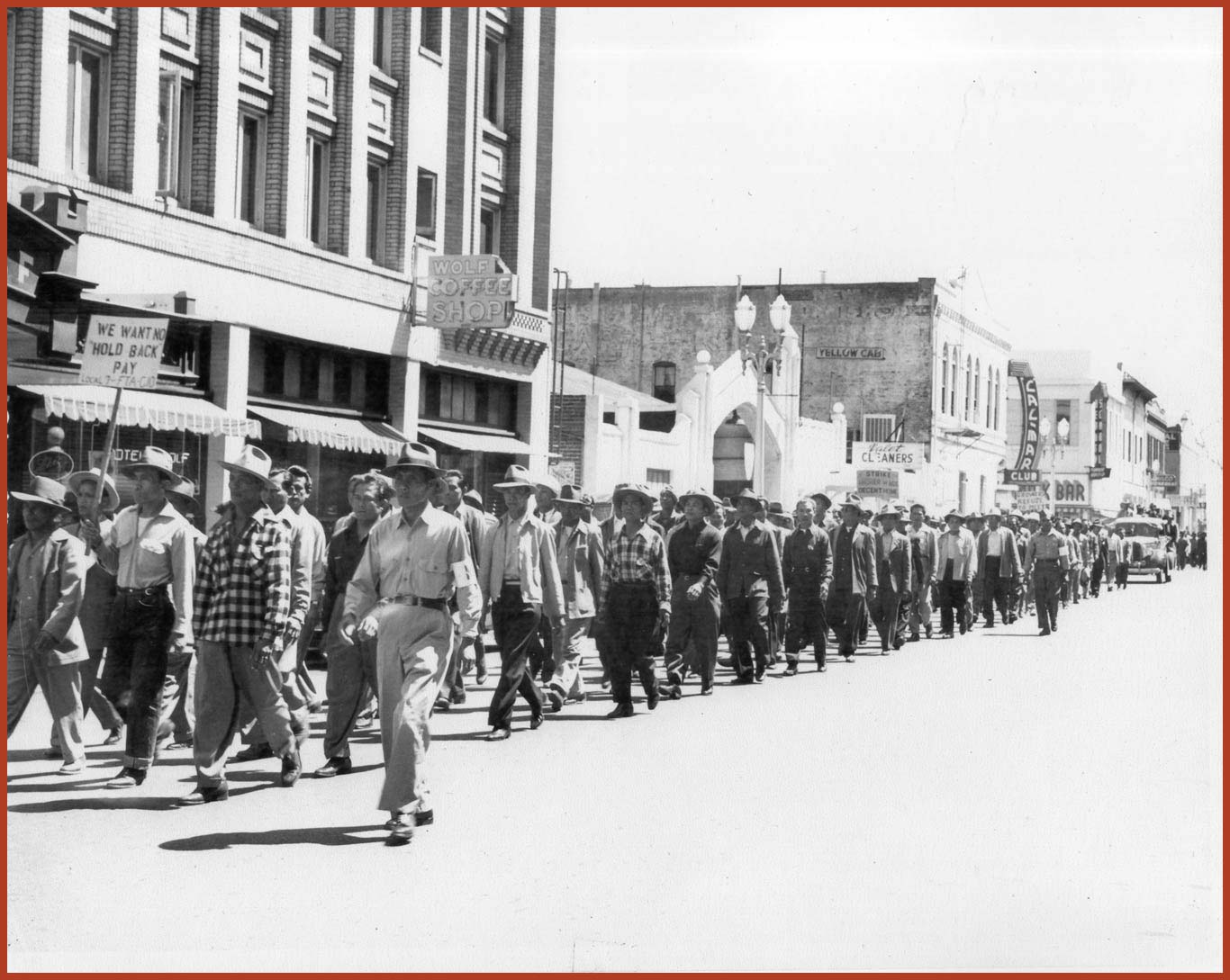 Individuals marching down a busy road holding signs. One of the signs read "We want no hold back pay."