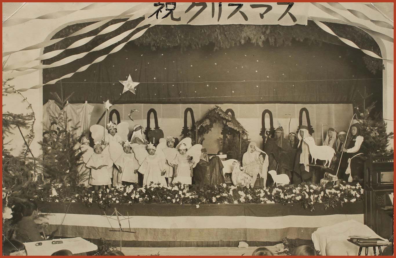 Black and white photo of young Japanese children dressed up as biblical characters to perform at a Church. There is a sign at the top of the stage written in Japanese.