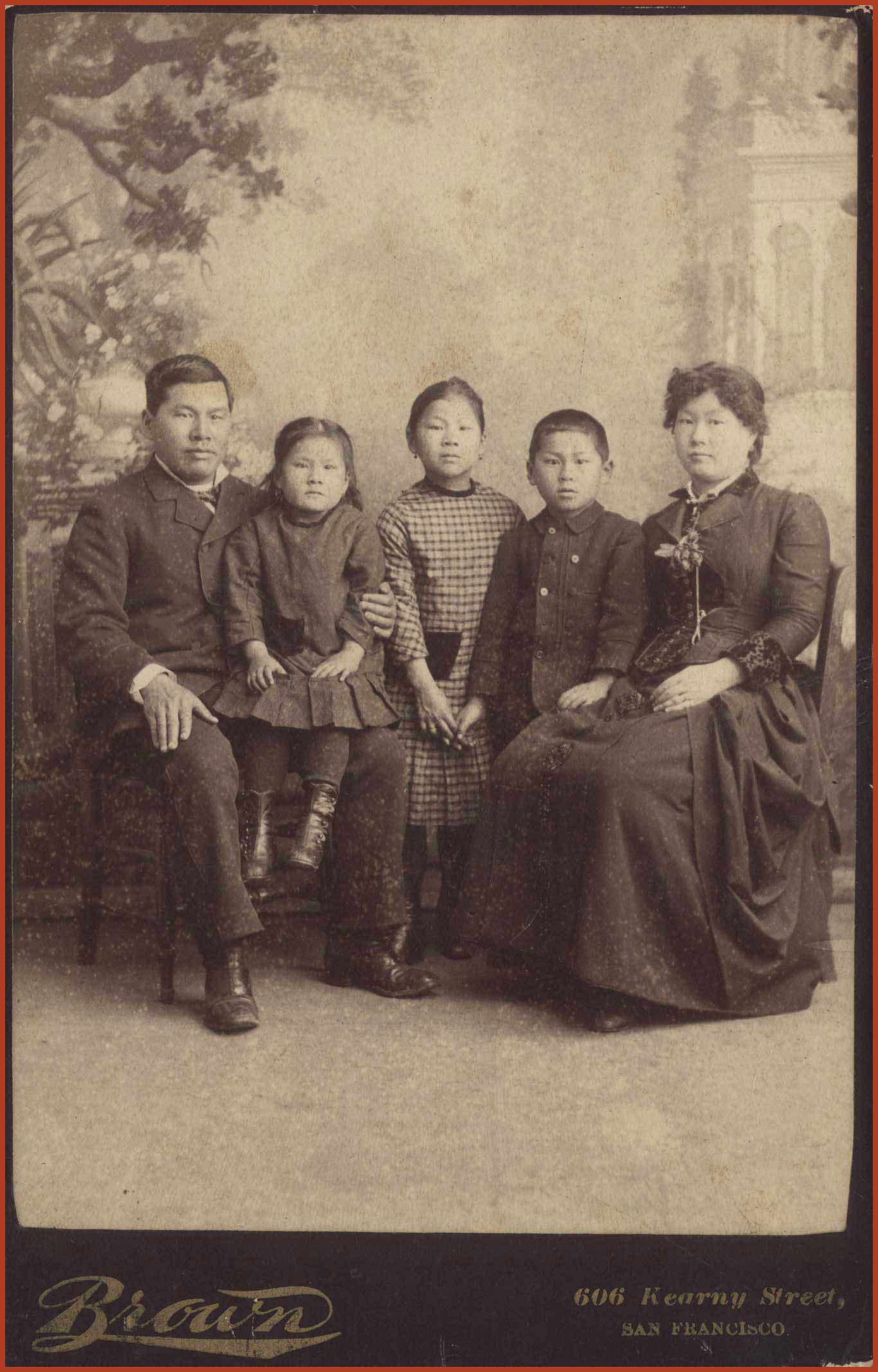 Family portrait of the Tape family in 1884. Joseph and Mary are sitting on chairs while Joseph has Emily on his lap. Mamie and Frank are sitting between them. Label at the bottom reads 'Brown, 606 Kearny Street, San Francisco.'