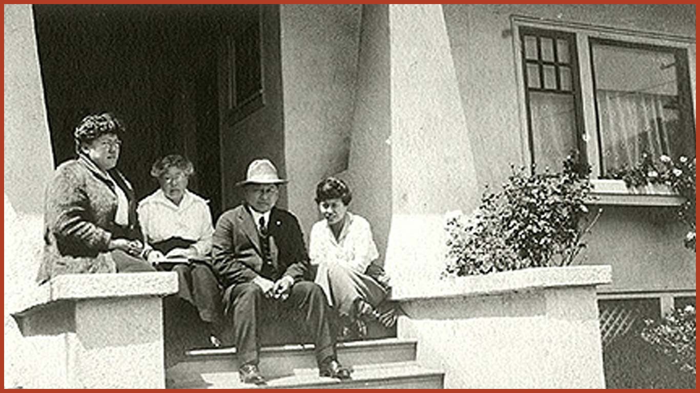 Black and white photo of a Chinese family sitting on the porch steps outside their home.