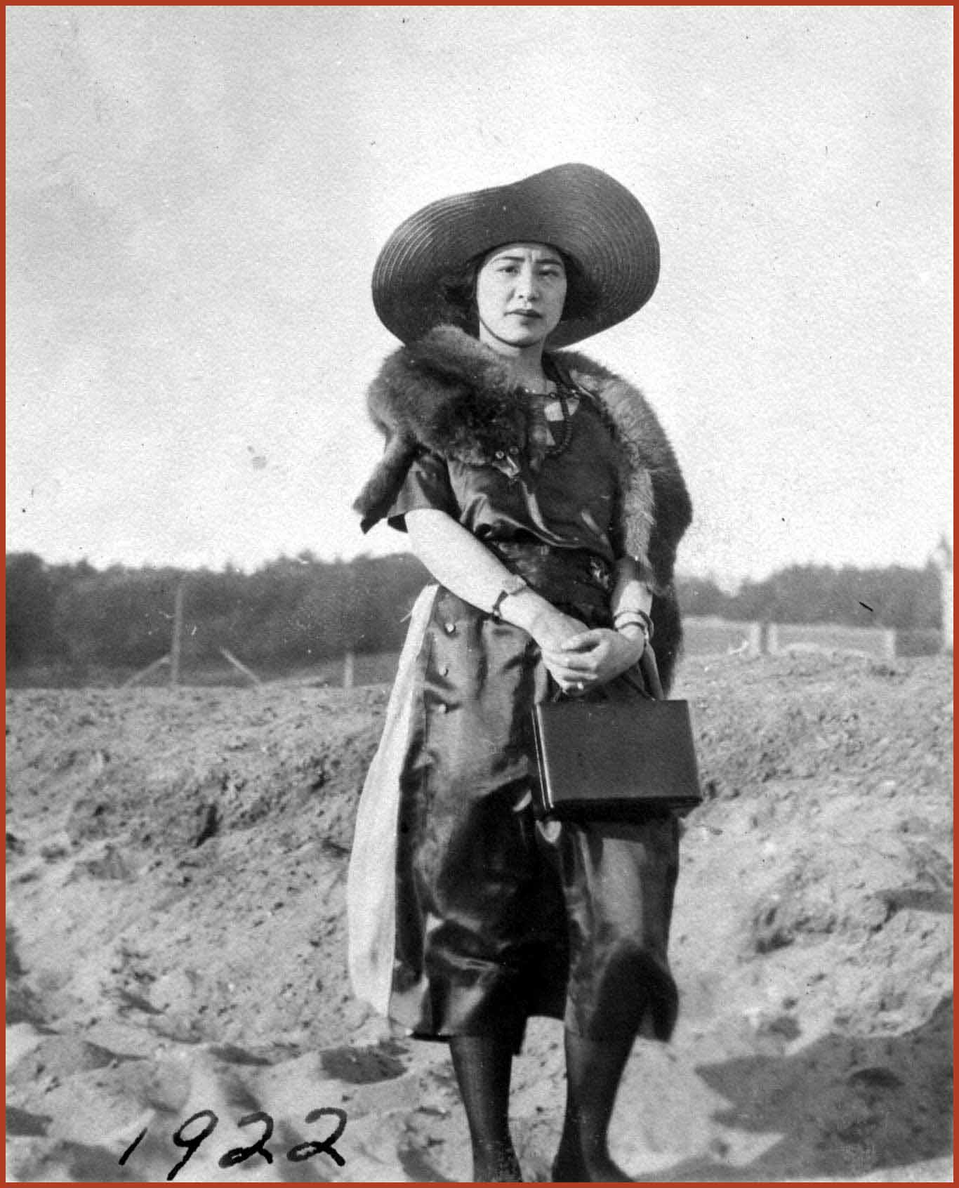 Black and white photo of a young Ruby Tape dressed in a hat and a fur scarf while holding a leather purse.