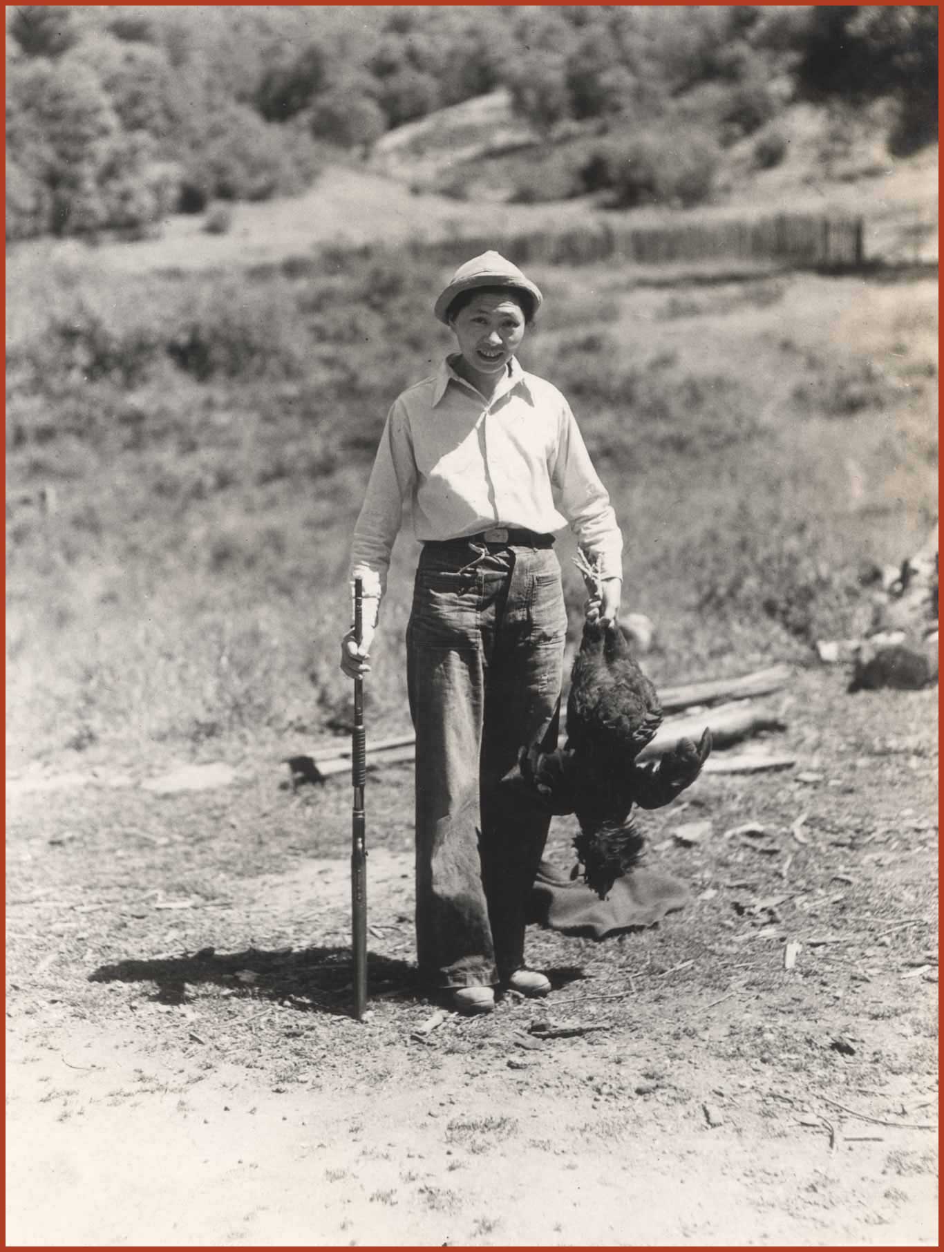 Black and white photo of Ruby Tape holding a hunting rifle and a bird she hunted.