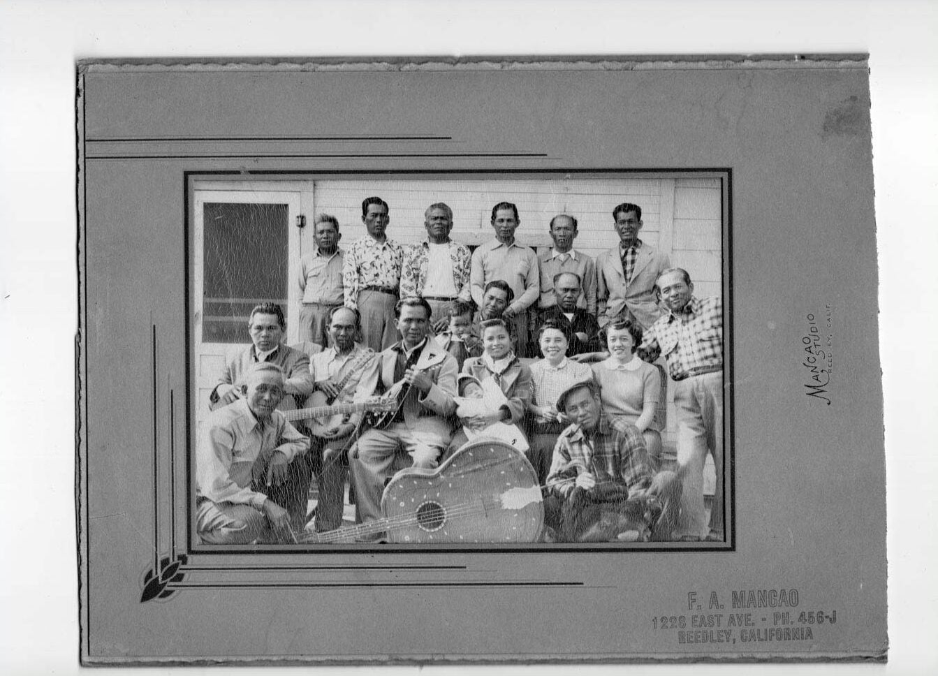 Group of 18 laborers sitting together smiling. Many are holding guitars, and one of the women is holding a baby.