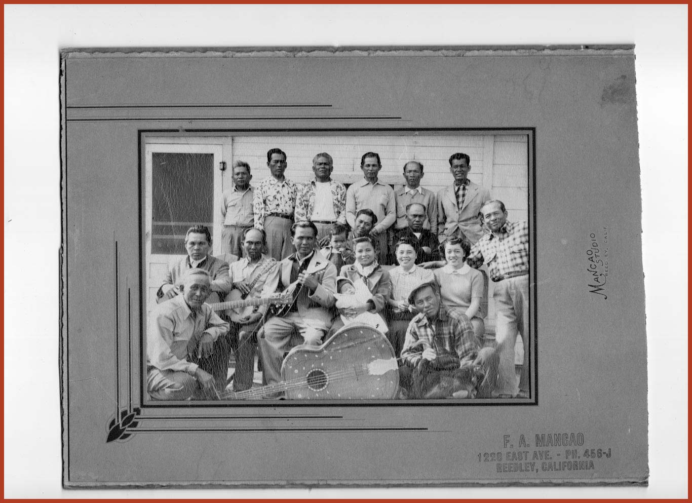 Group of 18 laborers sitting together smiling. Many are holding guitars, and one of the women is holding a baby.
