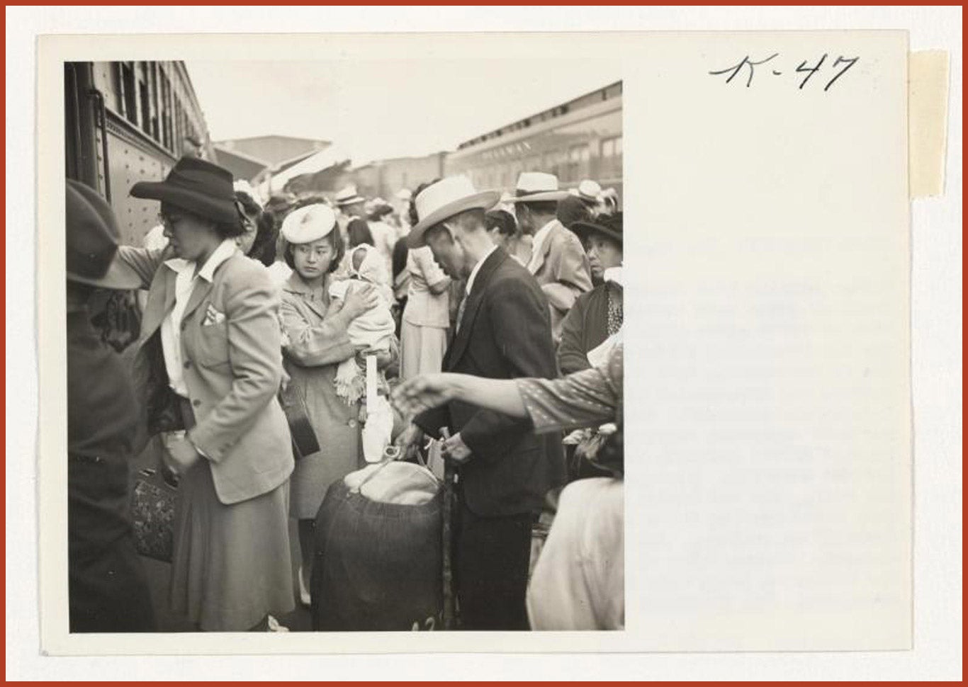 Crowds of Japanese Americans rushing to board the train. Center is a woman holding her child and a man grabbing their bag.