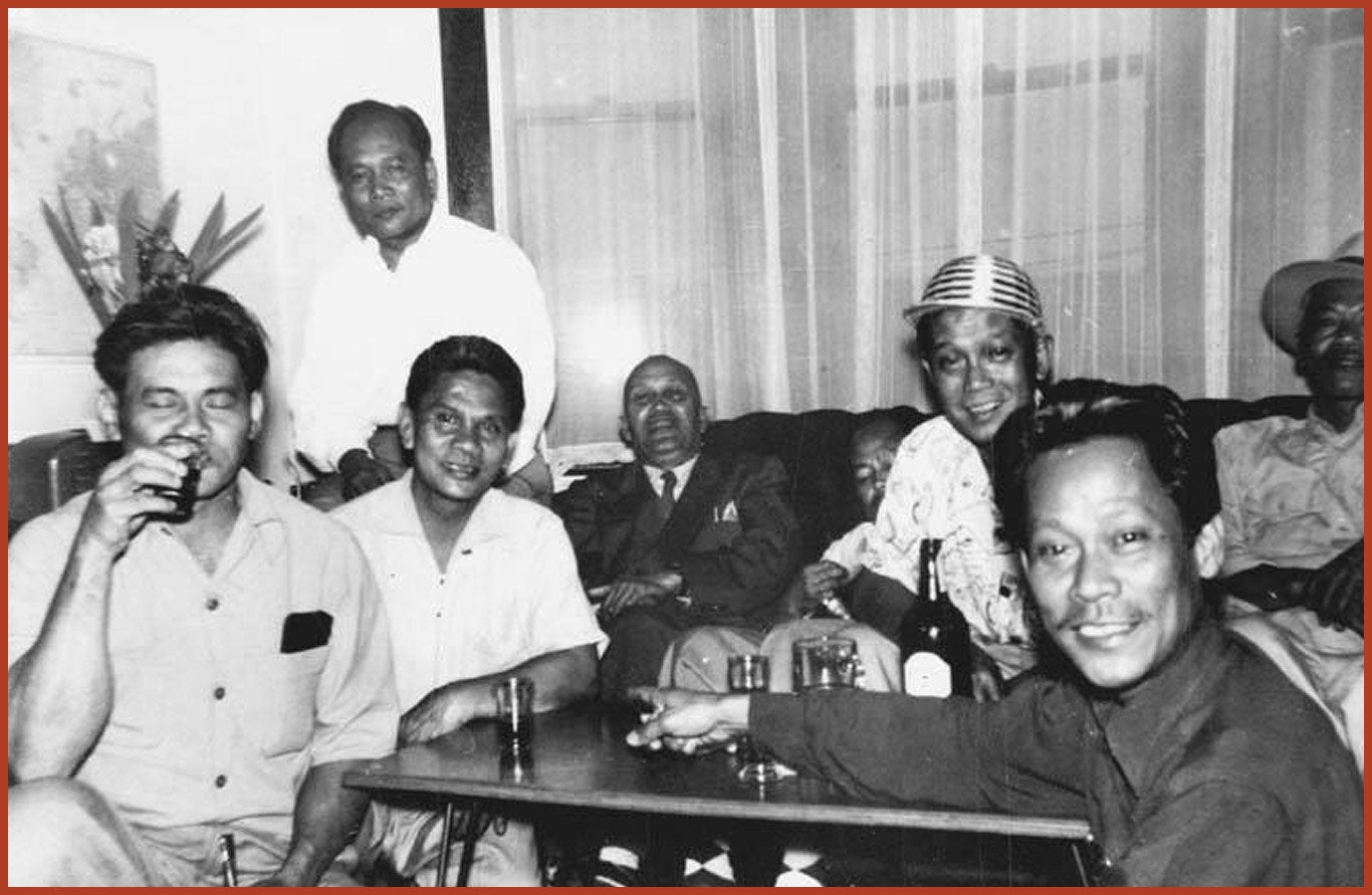 A group of men sit around a table leisurely, enjoying a drink.
