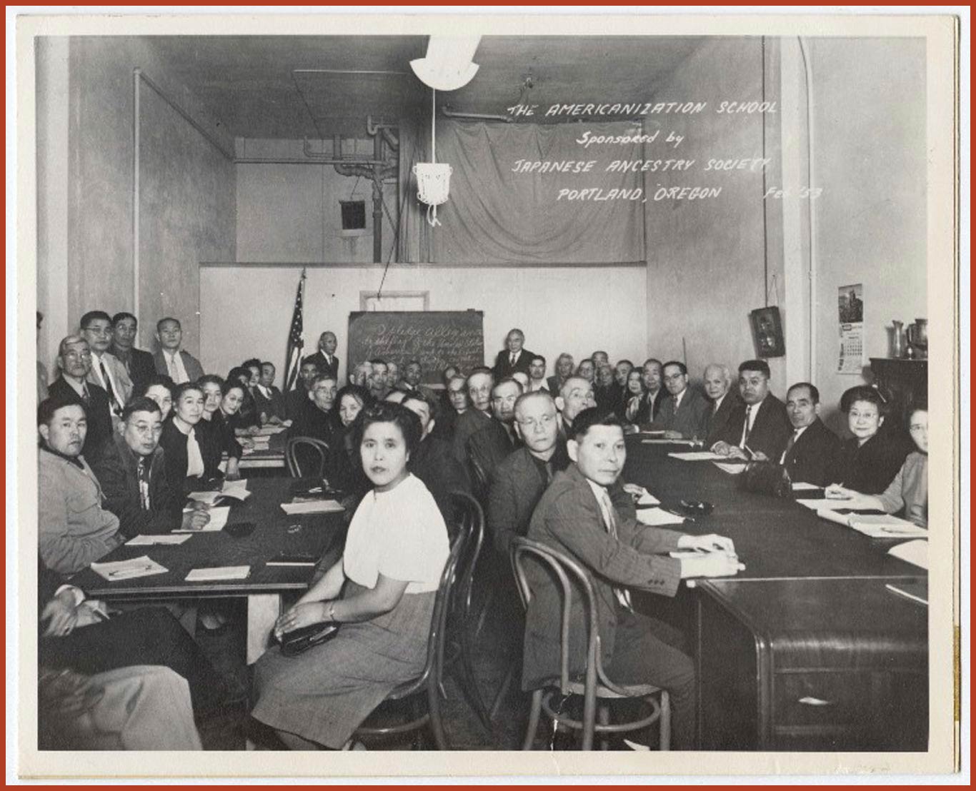 Black and white photo of two long sets of tables crowded with individuals in business suits and dresses. Label reads "The Americanization School sponsored by Japanese Ancestry Society, Portland, Oregon Feb '53."
