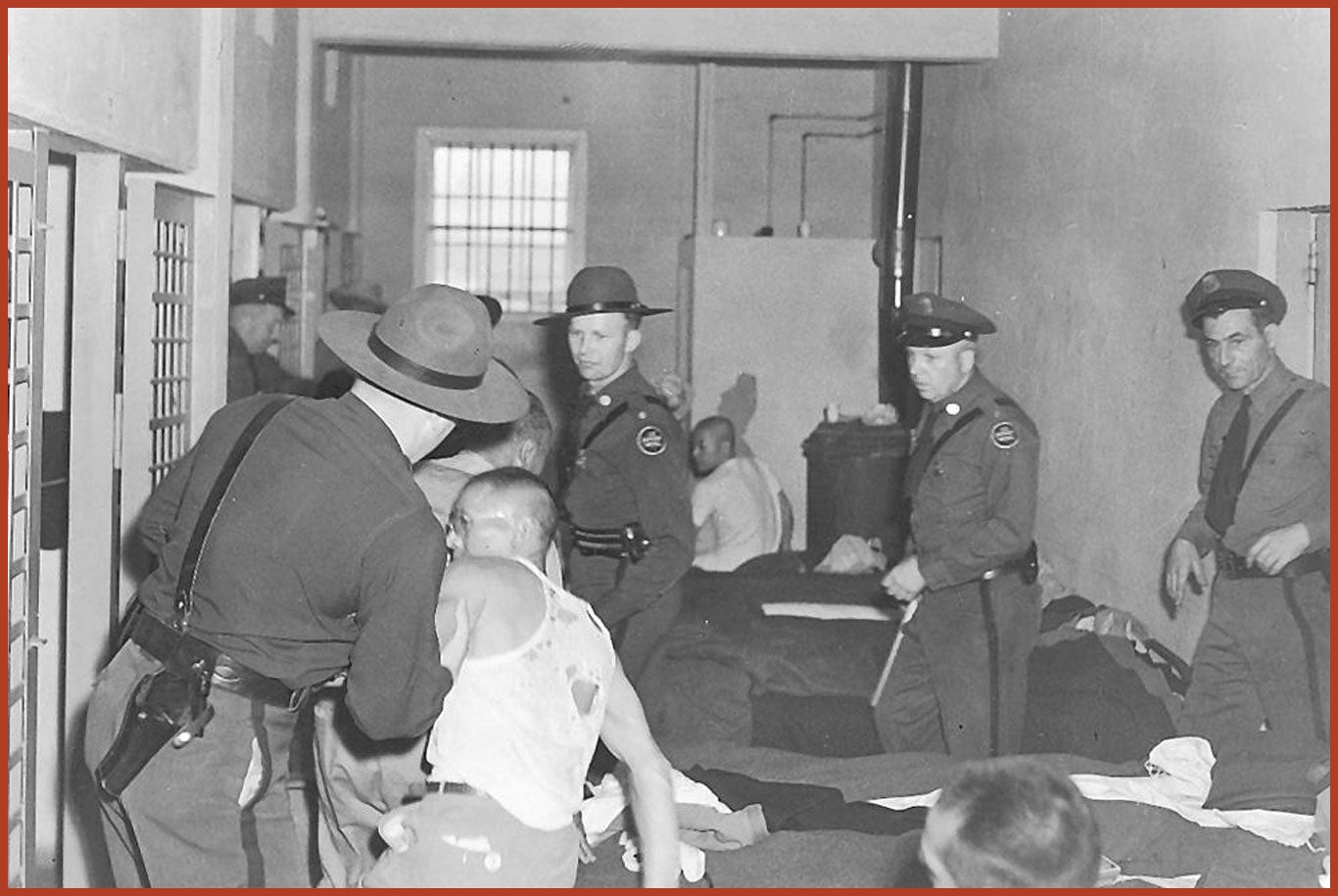 Several officers crowd around as an officer grabs an inmate in the Tule Lake jail. The inmates clothes are ripped.