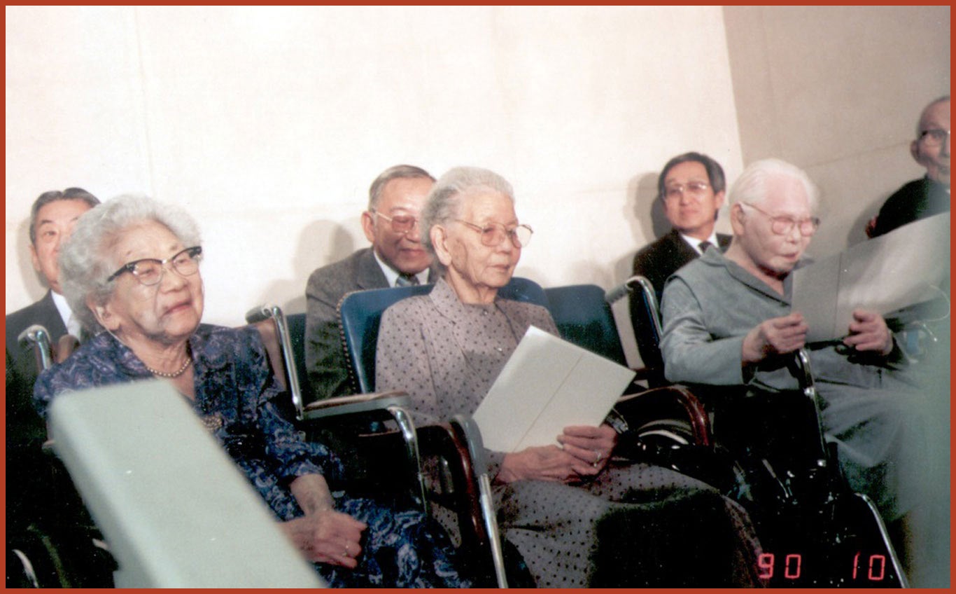 Group of elderly Japanese citizens sitting down while holding envelopes.