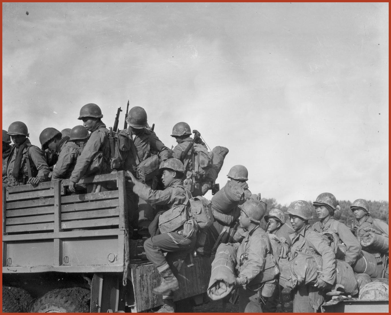 Black and white photo of Japanese-American soldiers loading into a truck with rifles and other equipment.