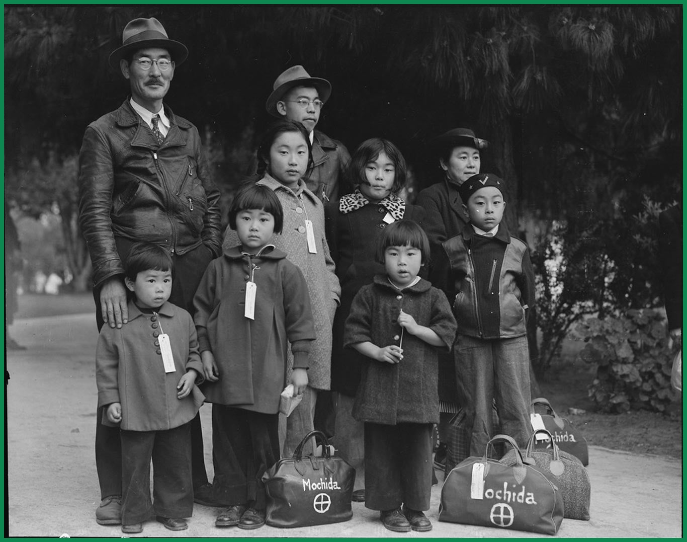 The Mochida family stands for a photo while waiting for the evacuation bus. Each member has a tag around their neck, and at their feet are three bags marked "Mochida."