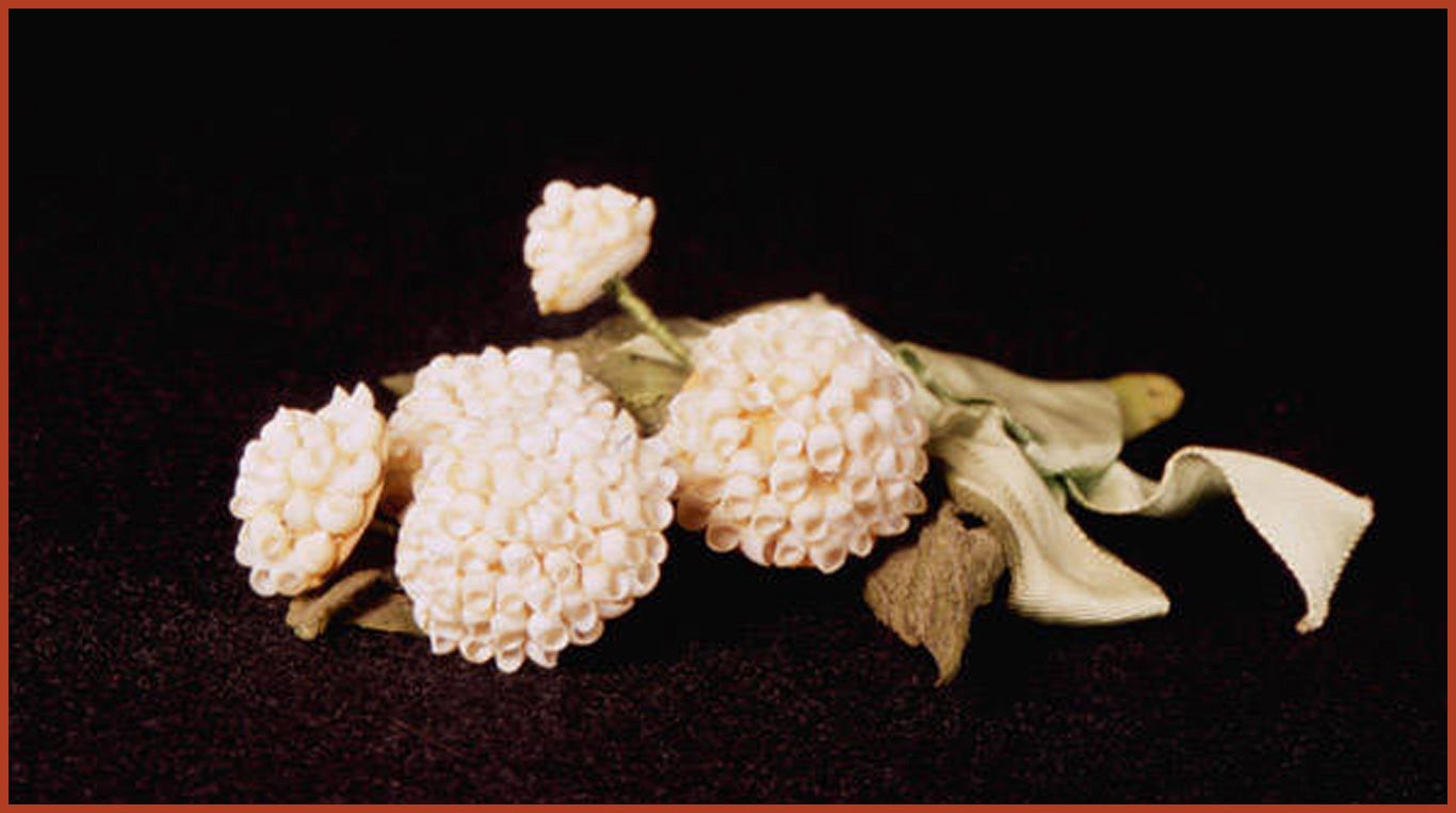 A white flower corsage made of shells, wrapped in green ribbon.