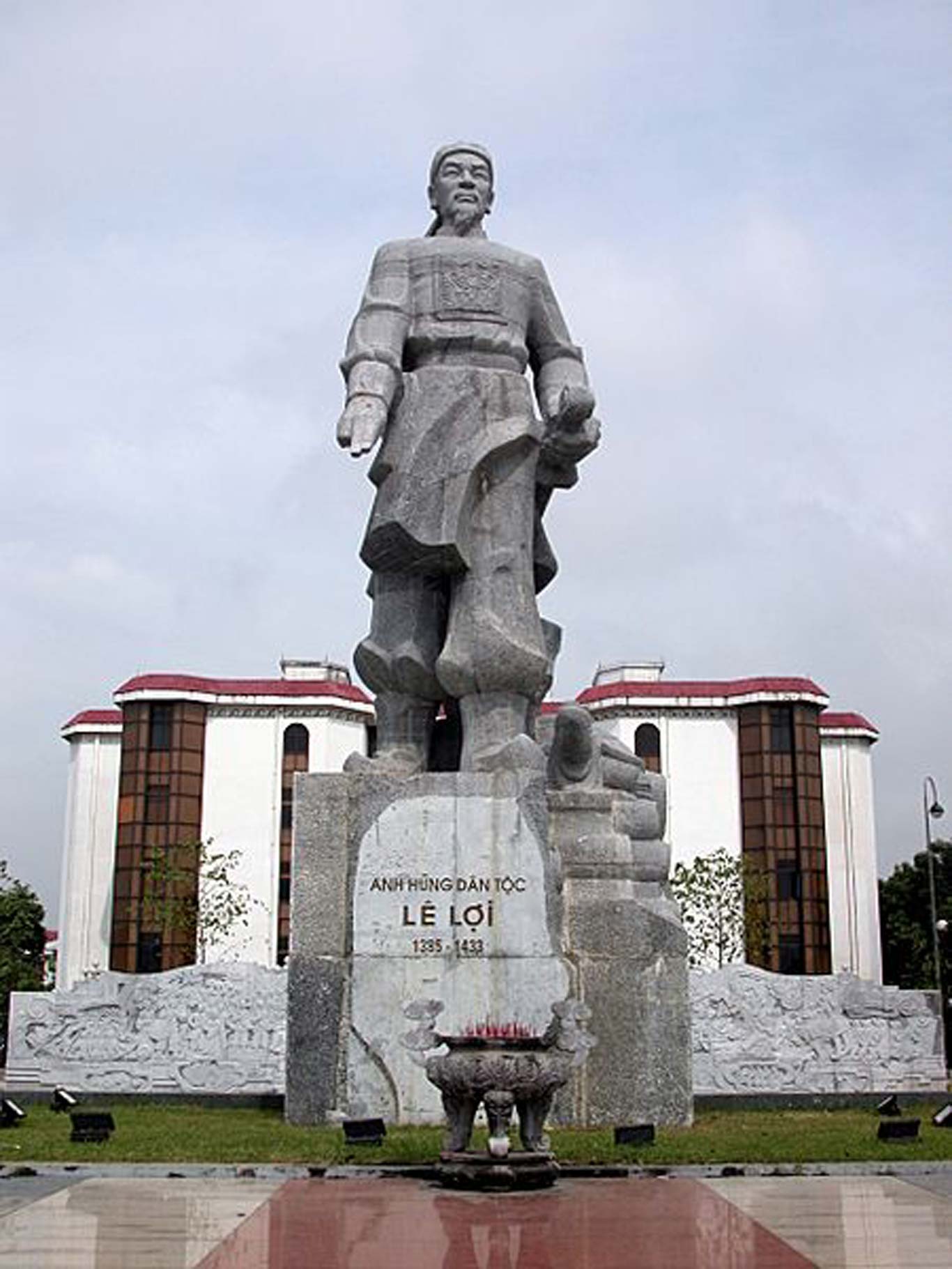 Statue of a Vietnamese man carrying a sword in one hand and holding out two fingers with his other. He is adorned in traditional Vietnamese clothing. Label reads "Anh Hung Dan Toc Le Loi 1395-1433".