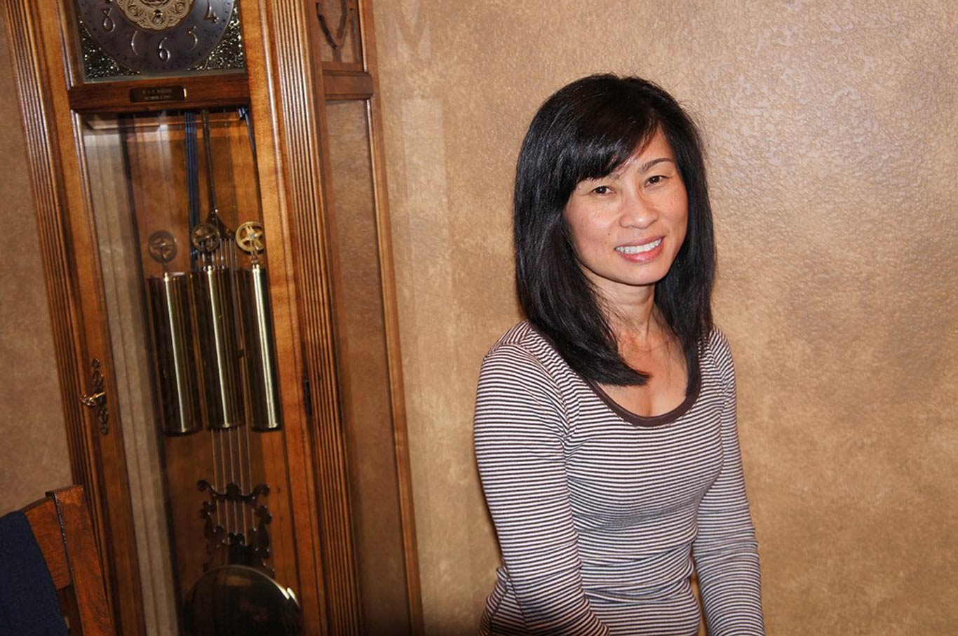 Quynh-Trang Nguyen sitting next to a large grandfather clock.