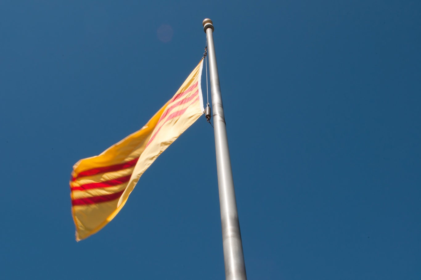 South Vietnam flag waving on a flag pole. The flag is yellow with three horizontal red stripes across the center.