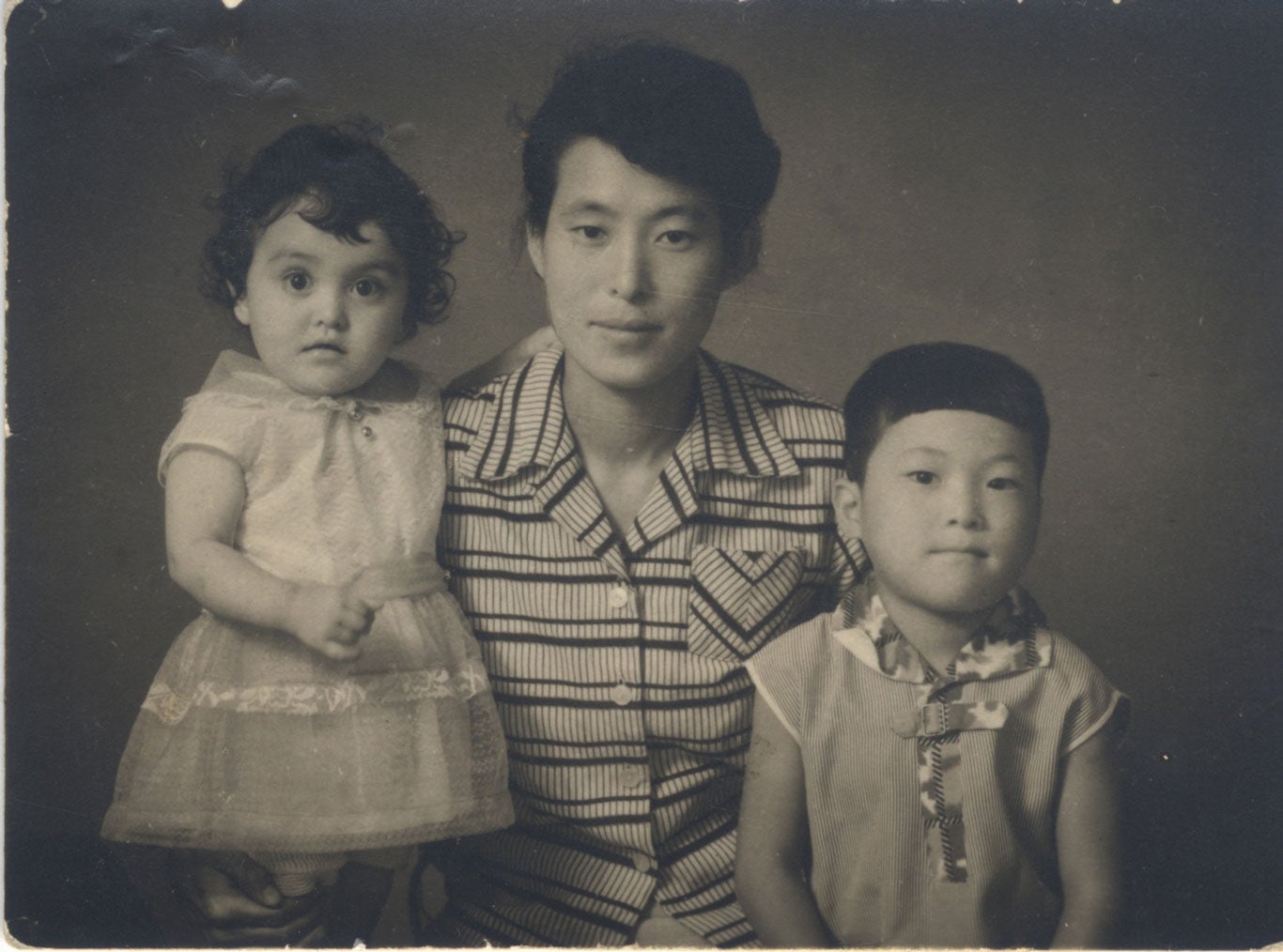Photo of a woman with a young girl and young boy on her lap.