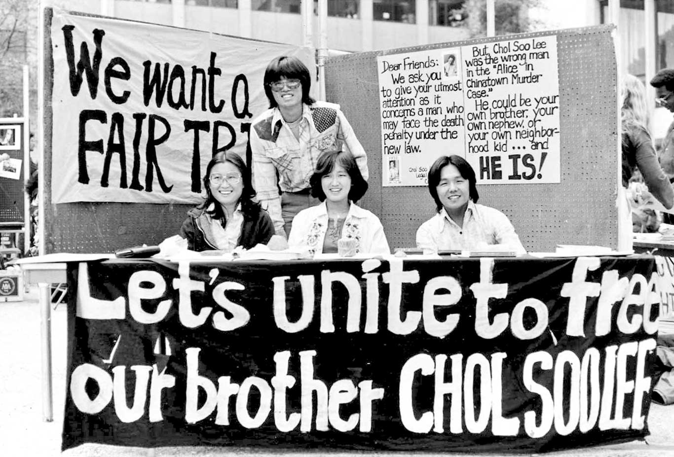 Four individuals gather around a table where a banner labeled 'Let's unite to free our brother Chol Soo Lee" hangs. In the back, a poster reads "Dear Friends, we ask you to give your utmost attention as it concerns a man who may face the death penalty under the new law. But, Chol Soo Lee was the wrong man in the "Alice in Chinatown Murder Case." He could be your own brother, your own nephew, your own neighborhood kid... and HE IS!"