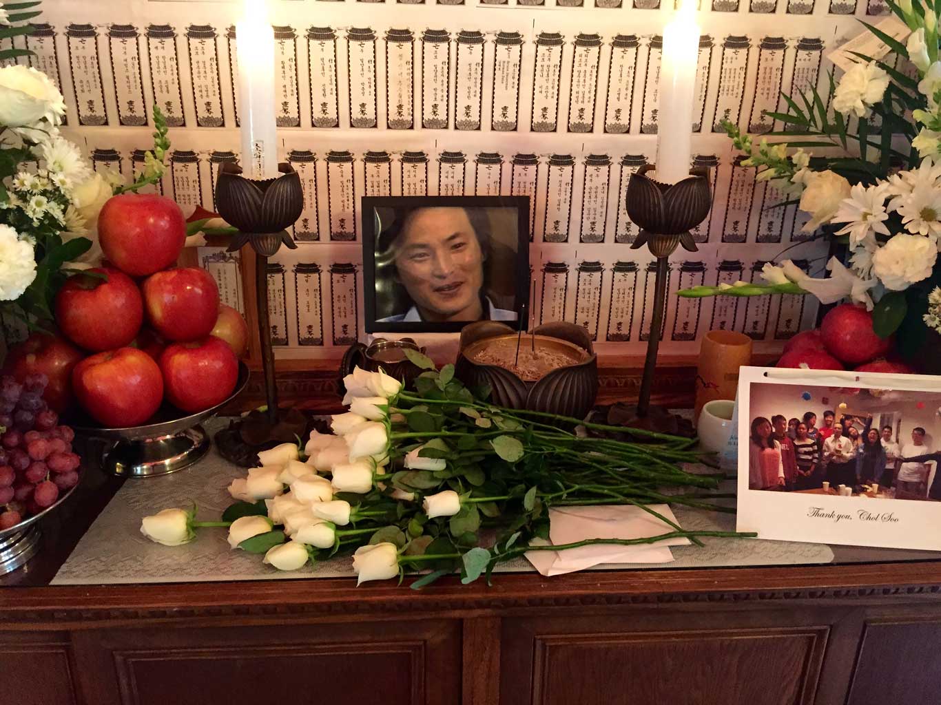 Photo of Chol Soo Lee on a table surrounded by flowers, candles and fruit.
