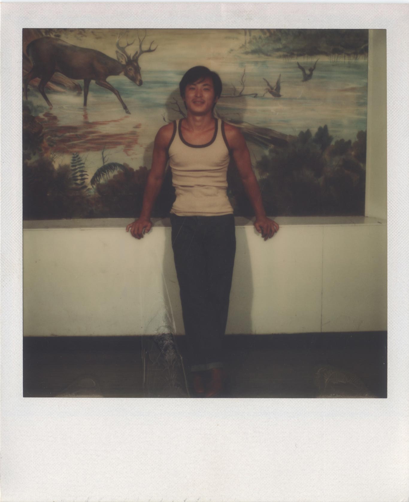 Chol Soo Lee smiling in front of a painted mural. The mural shows an elk in a river.