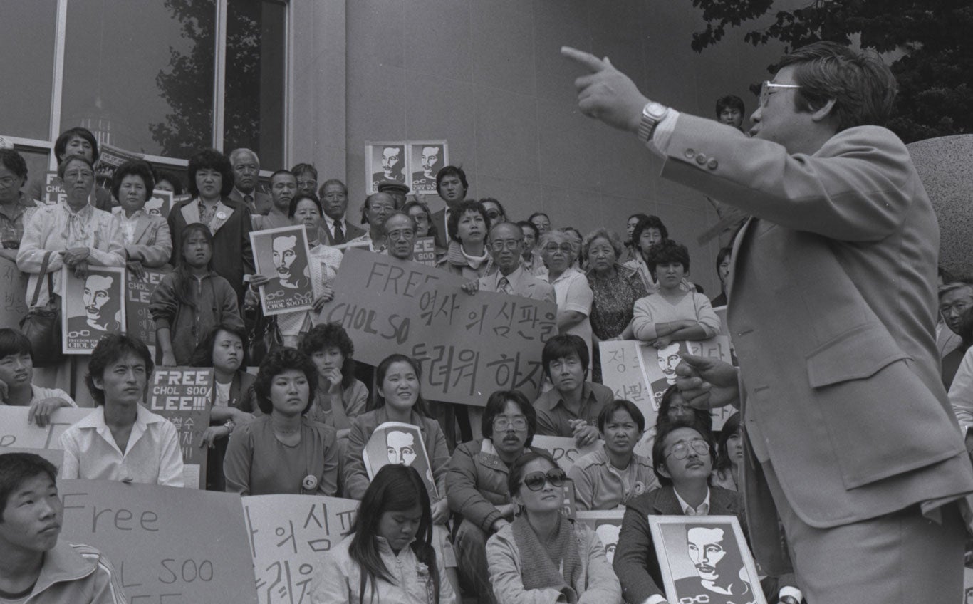 Man in suit speaks to a crowd of people gatheredwith signs that read "Free Chol Soo Lee" and otherswritten in Korean characters.