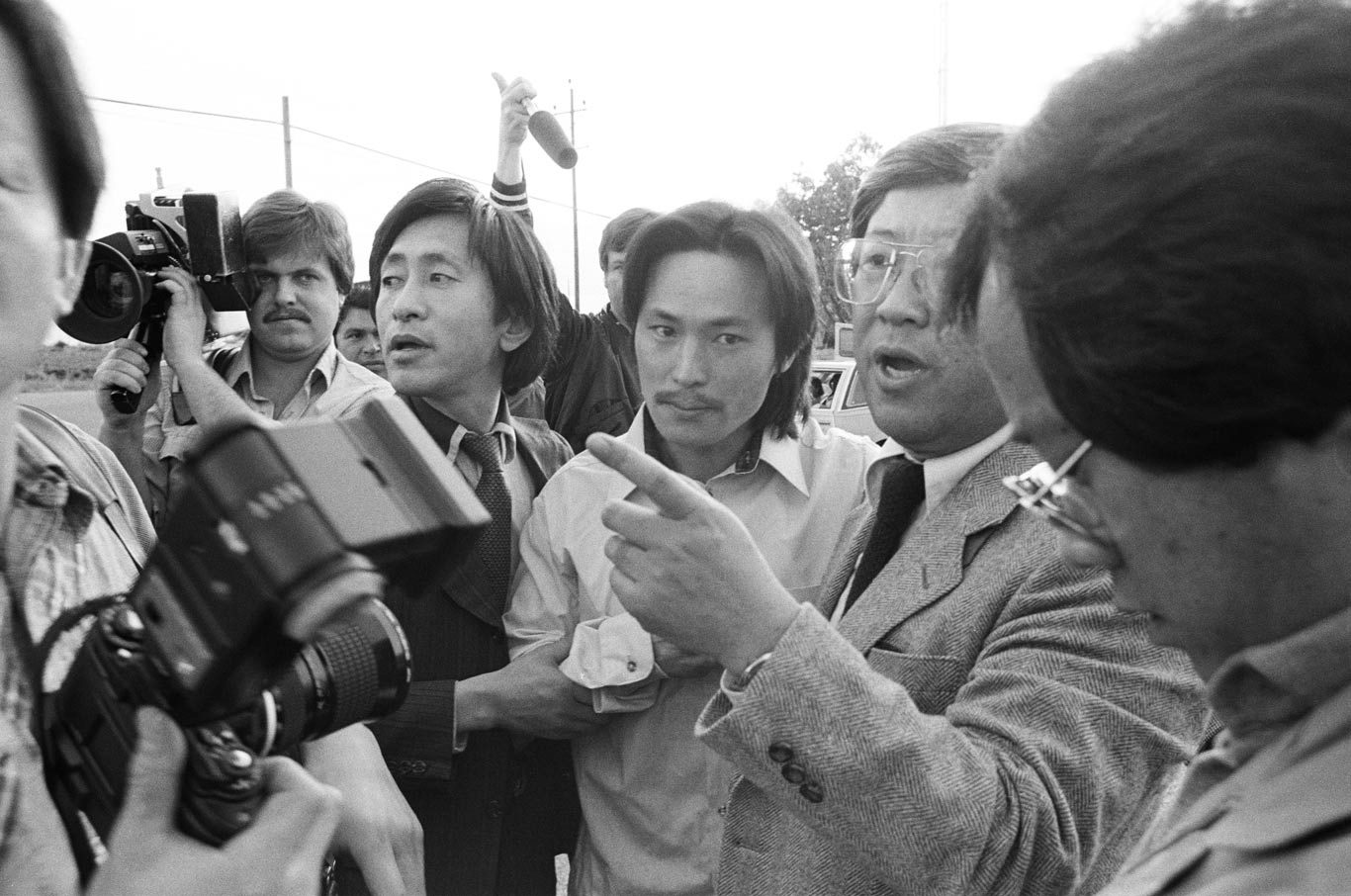 Chol Soo Lee walks with two men in suits while cameras surround them.