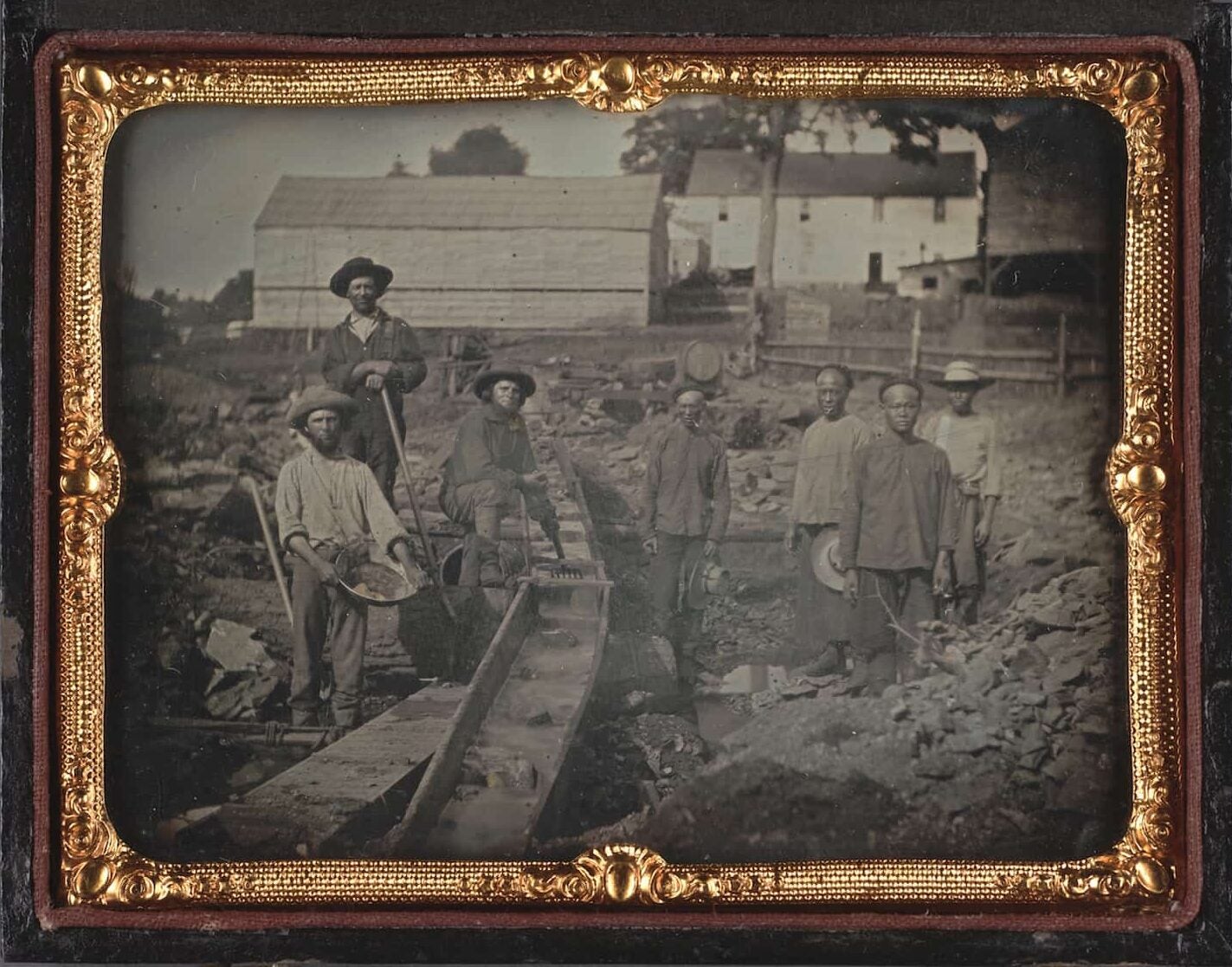 A framed photograph of a three white miners to the left of the sluice box and four Chinese miners to the right of the sluice box.