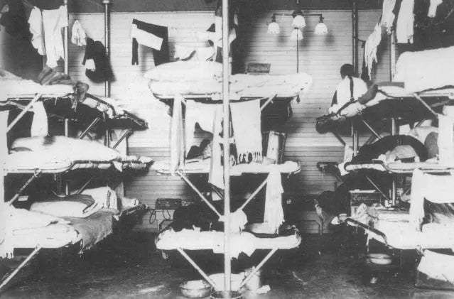 A small dormitory on Angel Island shows detained Chinese immigrant men laying in cots tightly packed and stacked together.