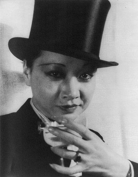 Portrait of Anna May Wong wearing black tophat and holding a glass.
