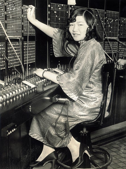 Chinese American Harriett Ng dressed in a Chinese dress operating a telephone system.