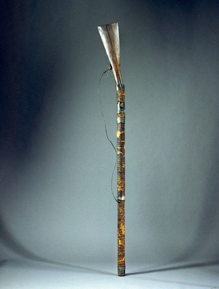 Exhibit photo of a homemade gun from the Philippines. Wood carved handle with a long, narrow barrel and attached strap.