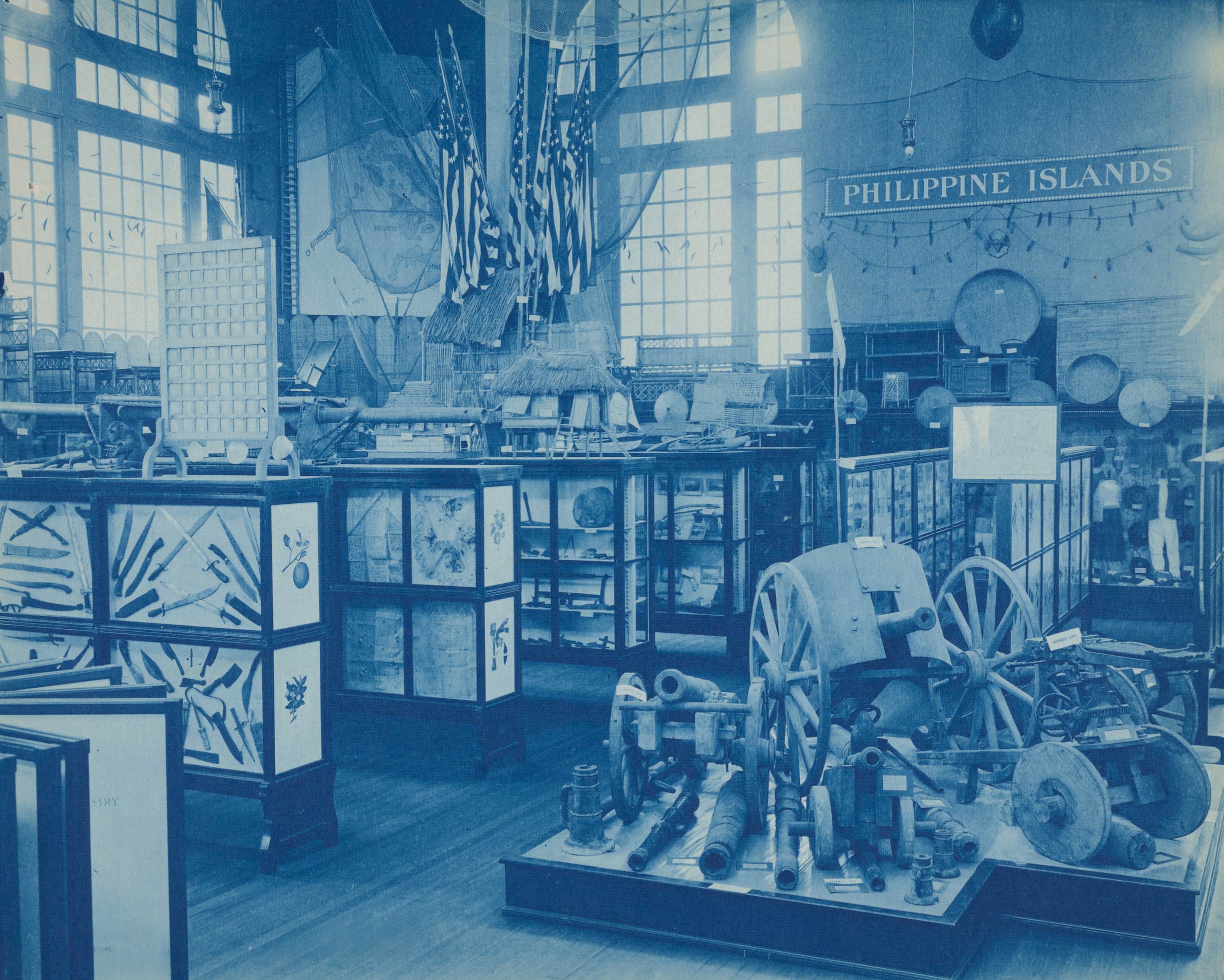 Philippine Islands exhibit booth displaying agricultural machinery, tools, maps, flags and cookware.