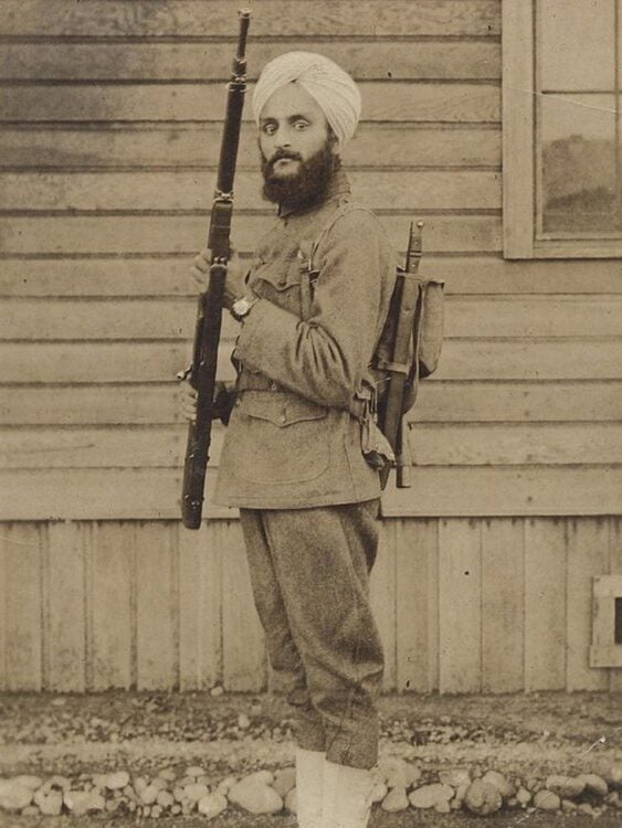 Bhagat Singh Thind, a Sikh man, in his U.S. Army uniform and turban, standing at attention with his rifle and gear.