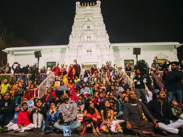 Devotees sit on steps in front of the Sri Venkateswara Temple all looking up at the fireworks show.