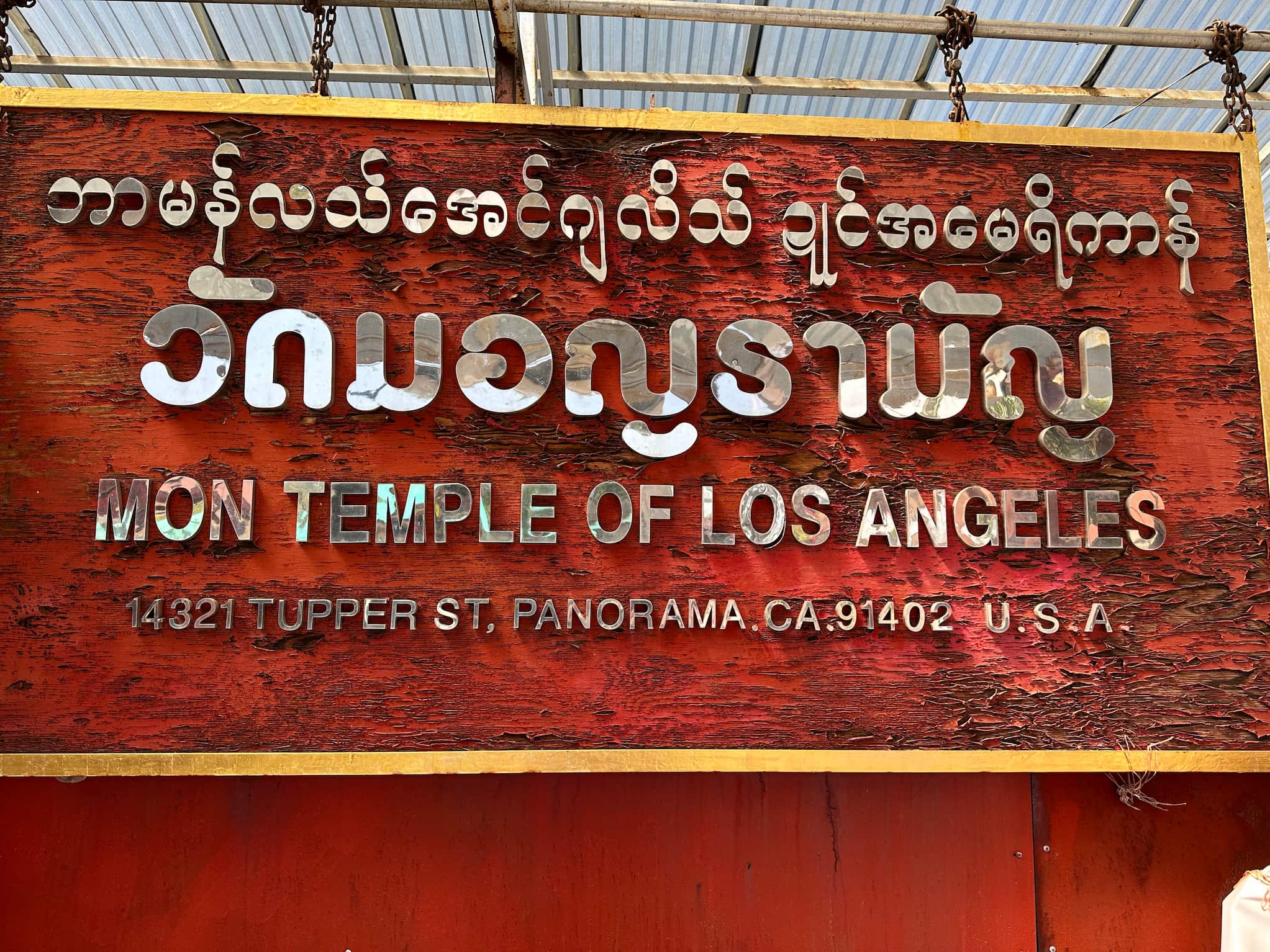 Hanging sign with reflective lettering. Text in English reads "Mon Template of Los Angeles" with address below. Mon and Thai script appear above.