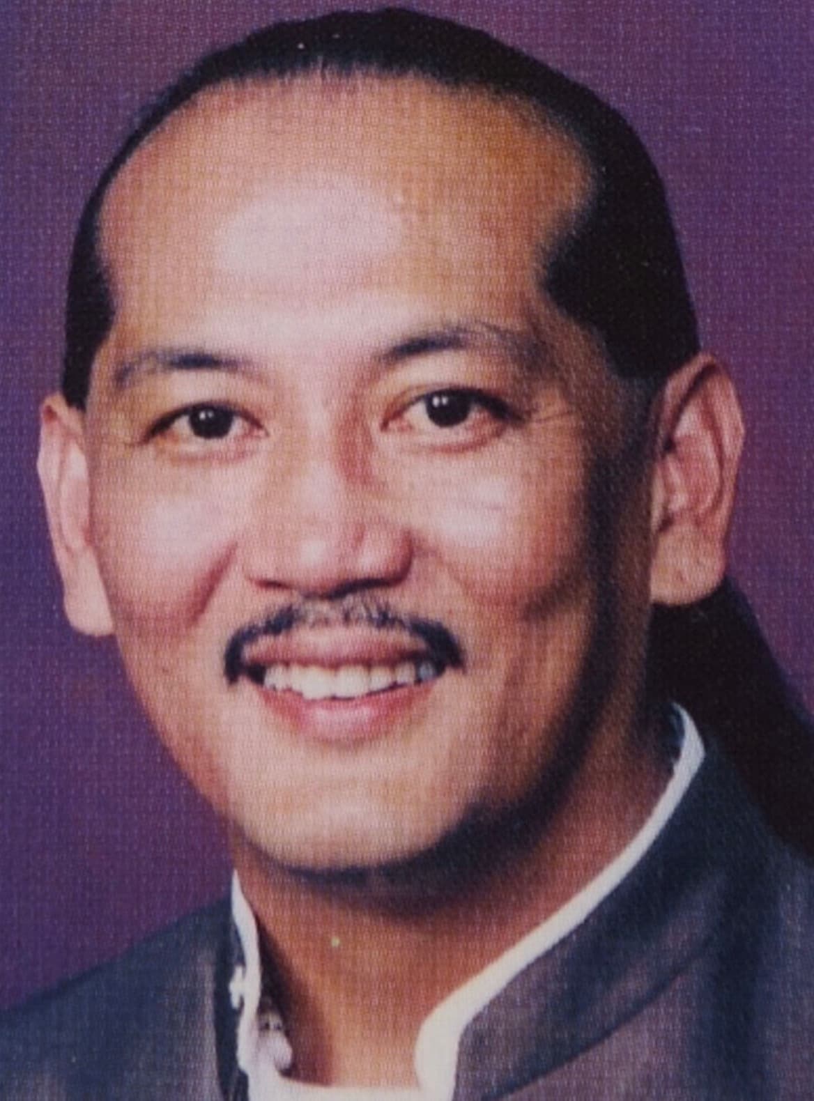 Angel Ånghet LG Santos, a Chamorro rights activist and Guamanian politician with long, black hair, smiles for portrait against purple backdrop.