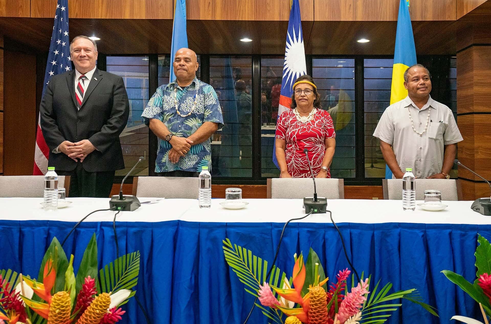 Micronesian leaders and U.S. Secretary of State stand for group photo behind press conference table. Flags from each respective country hang behind.
