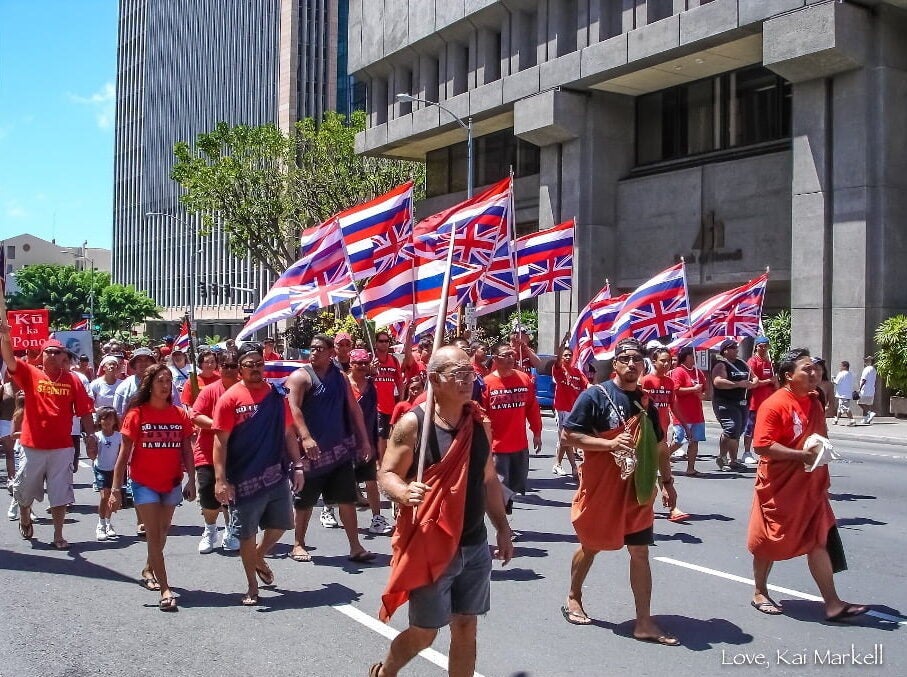 Advocates of Hawaiian independence, dressed in matching Kū I Ka Pono t-shirts, march down the street holding Hawaiian flags.
