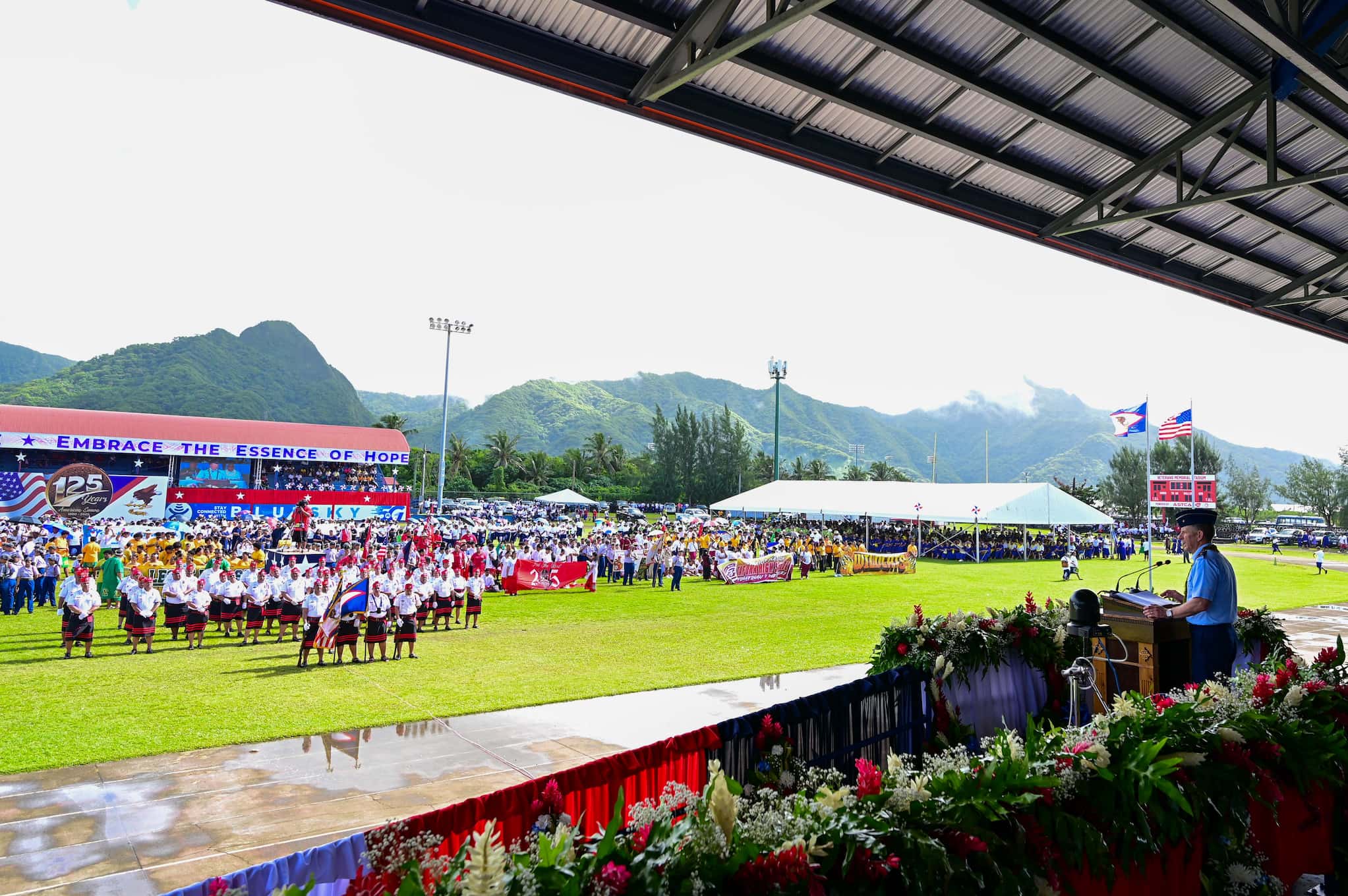 Brigadier General W. Alan Matney stands behind a podium under a shaded outdoor stage while addressing an audience of Samoans and Fita Fita Guards.