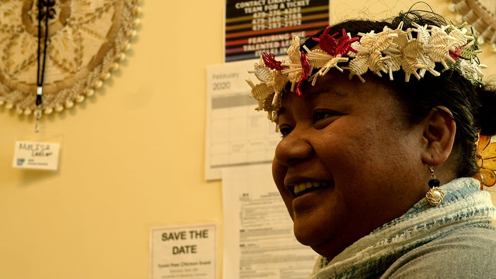 Melisa Laelan, wearing a handwoven floral garland around her head, smiles at work in indoor candid.