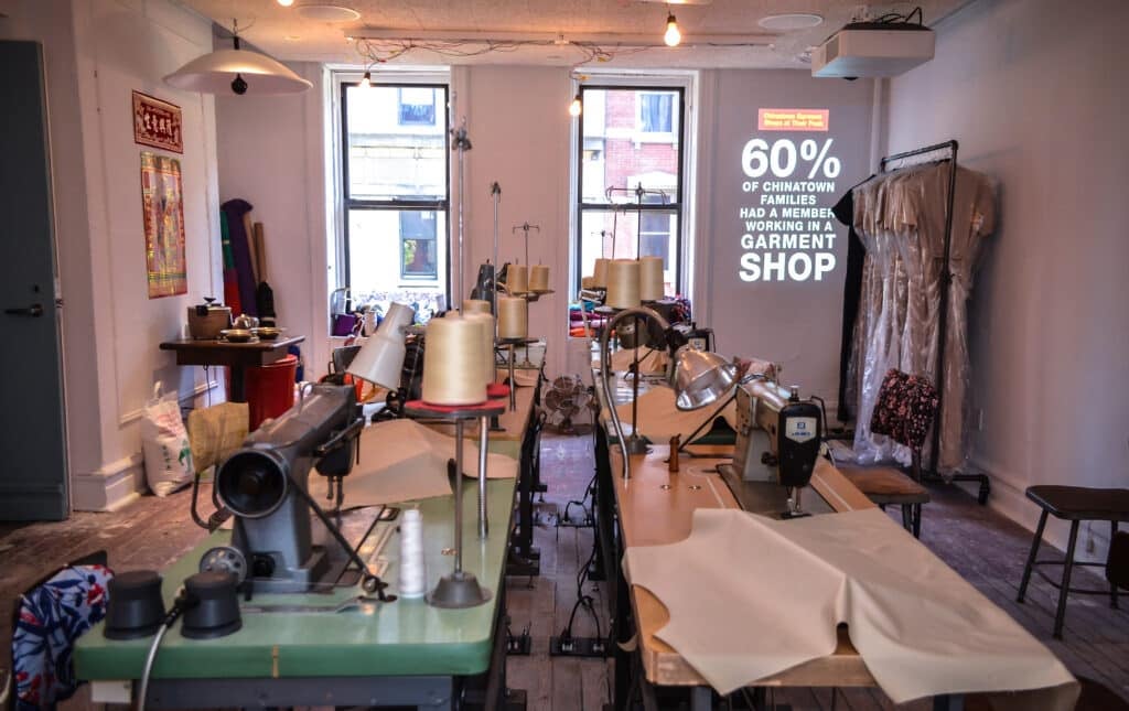 Museum exhibit depicts a typical sewing factory from the 1980s, showing a small room with multiple tables, sewing machines, and clothing racks.