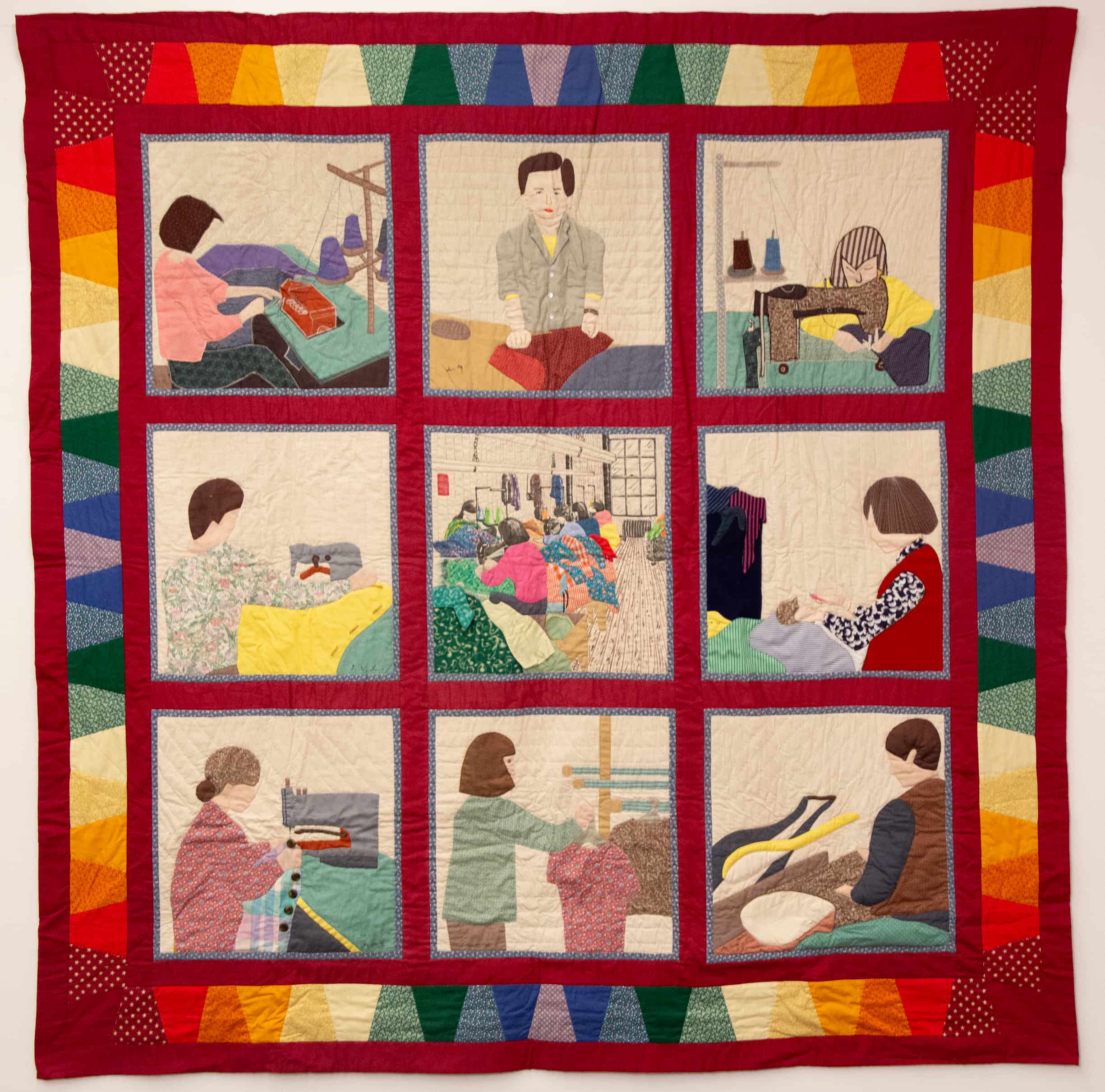 Colorful quilt sewn by garment workers. Ringed with red fabric, the quilt has nine squares, each with different scenes.
