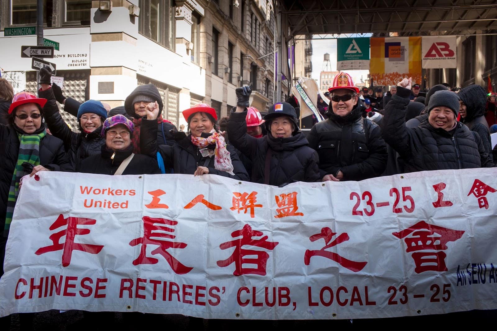 Factory worker retirees stand behind "Chinese Retirees' Club, Local 23-25" banner in outdoor march for Triangle Shirtwaist Fire Commemoration.