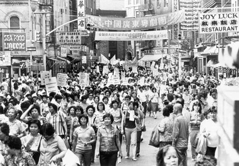 Large crowd of people march through Chinatown street.