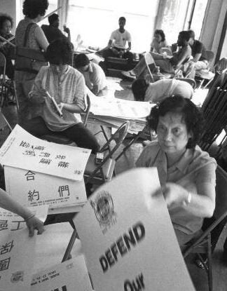 Volunteers, seated around tables, prepare signs in English and Chinese ahead of rally. One sign reads "Defend Our Union Contract."
