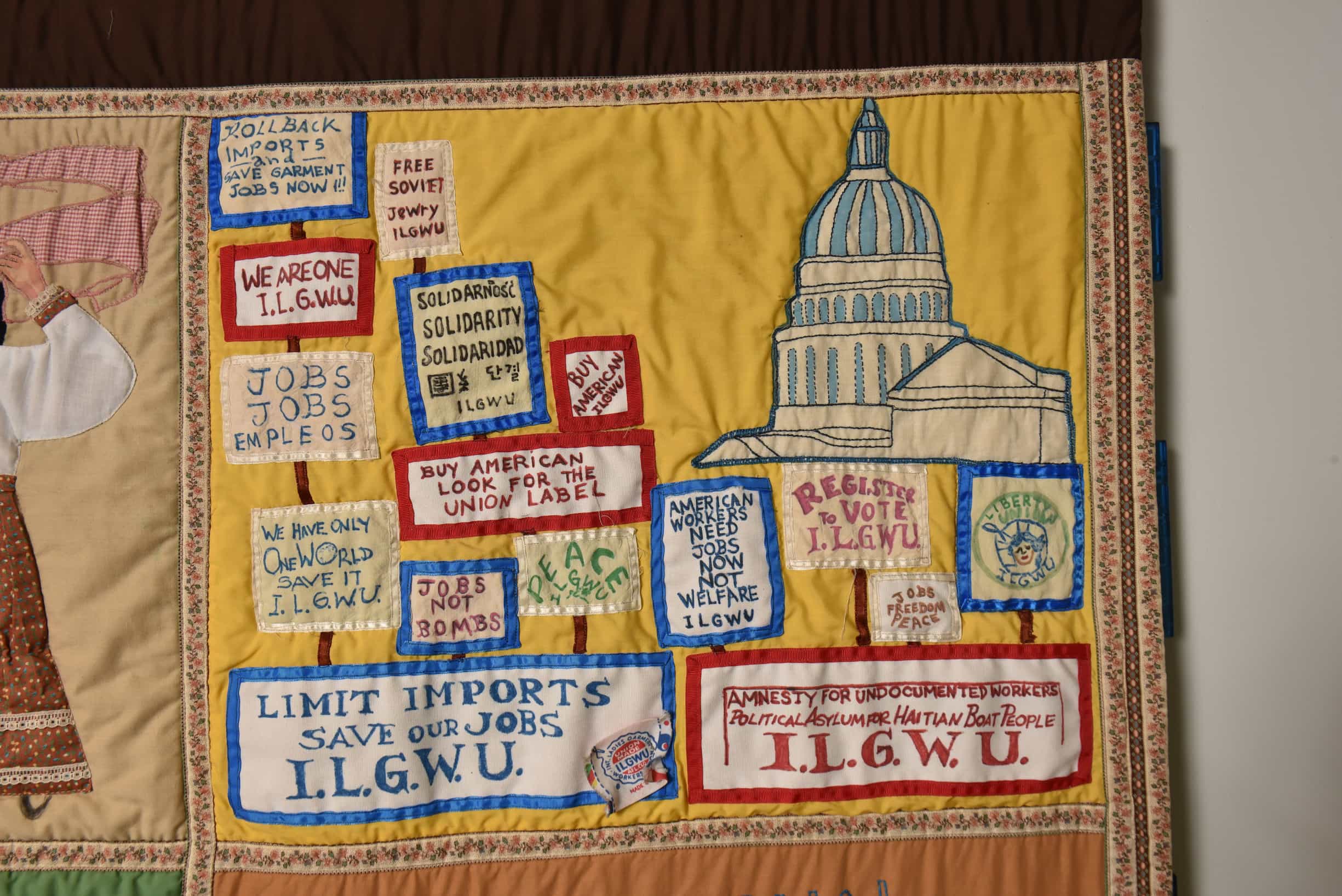 Close up on quilt square with yellow background. The U.S. Capitol Building is shown with ILGWU protest signs in front of it.