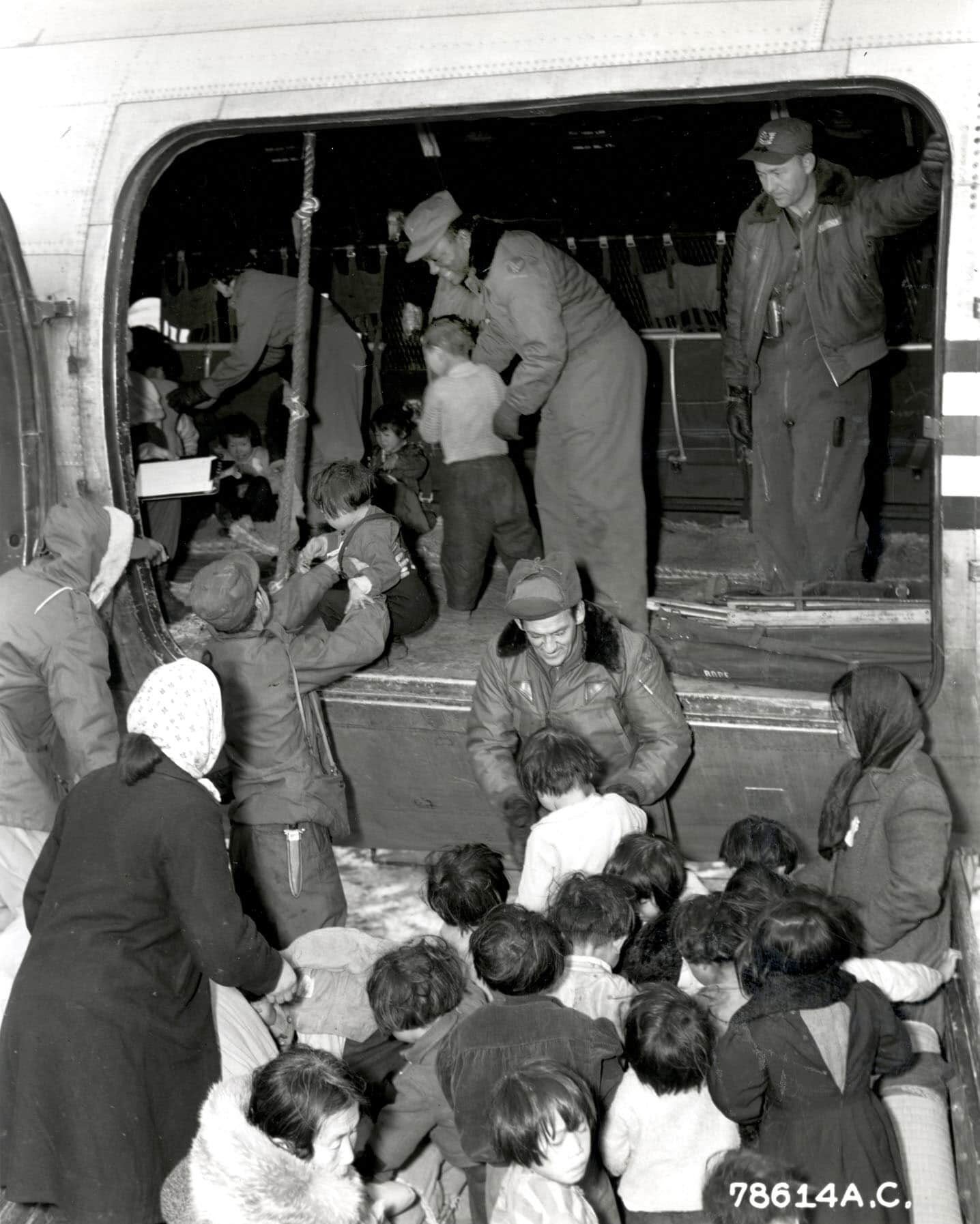 Uniformed members of the U.S. Air Force lift Korean children into plane cabin.
