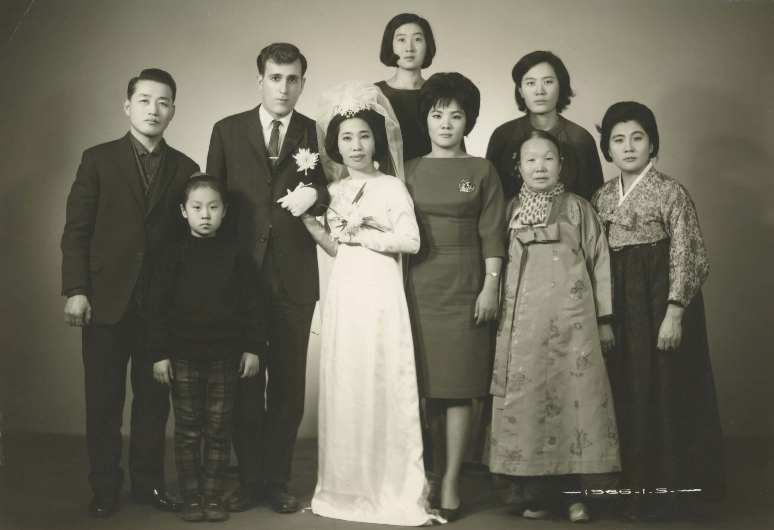Formal wedding portrait of a Korean military bride posing with her white American husband, surrounded by the bride's family.